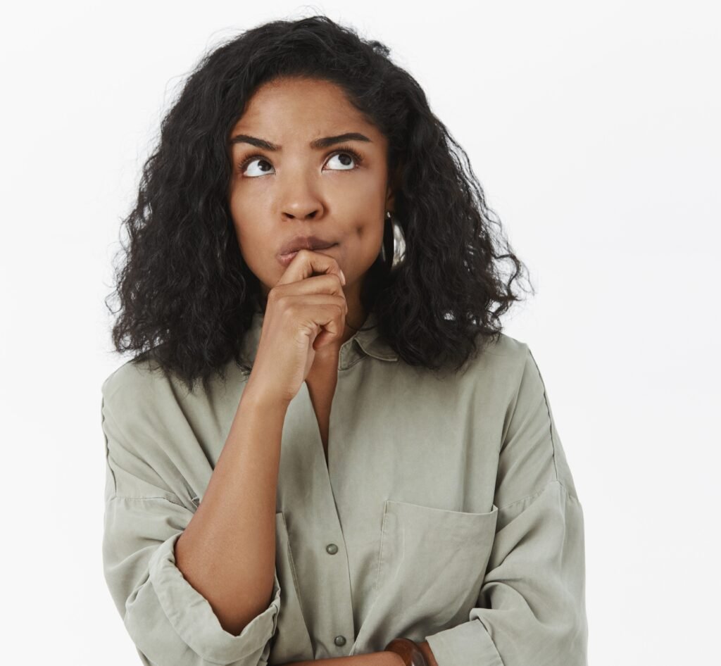 Girl needs make up excuse thinking standing focused in thoughtful pose holding hand on chin frowning looking up posing over gray background determined and concentrated on thought